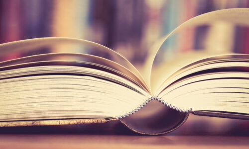 Close,Up,Opened,Book,Page,With,Blurry,Bookshelf,Background,For